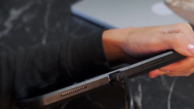 Close-up of hand inserting USB-C cable into tablet port for charging and data transfer, modern gadget usage, portable device connection, everyday tech routine at home or office