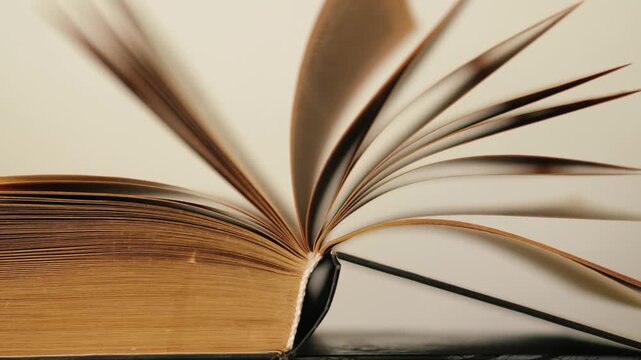 Macro shot of an open vintage book with pages flipping smoothly. Close-up of weathered yellow paper and book spine with turning pages in soft light.