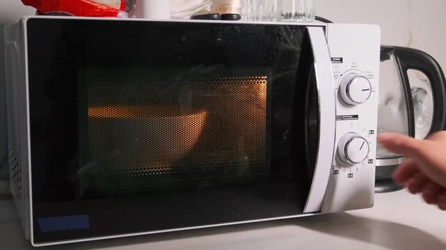 Close-up of a hand turning the rotary knob to start a microwave oven, setting cooking time and heating food in a modern kitchen appliance. Using microwave oven with rotary control