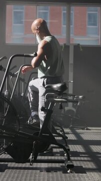 Exercise, bike and black man in gym, phone to track progress and workout for health benefits. Cycling, mobile user and old person in wellness facility, fitness and digital app to review membership