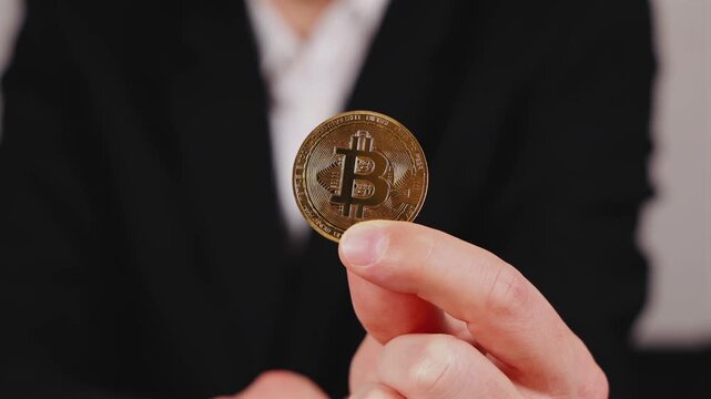 Une personne en train de montrer un bitcoin. En arri&egrave;re plan, elle est habill&eacute;e en costume.