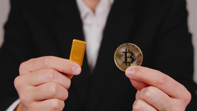 Une personne tient une pi&egrave;ce de Bitcoin et un lingot d'or dor&eacute;e dans ses mains. En arri&egrave;re plan, une personne en costume et chemise blanche. Concept de bitcoin vs or.