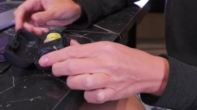 Close-up of hands taking wireless sports earbuds out of a charging case, showing portable audio device usage, charging process and preparation for listening in everyday activity