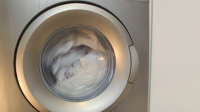 washing machine drum rotating clothes front view, continuous spin cycle moving fabric inside appliance, active washing process with water motion, household laundry routine and cleaning operation
