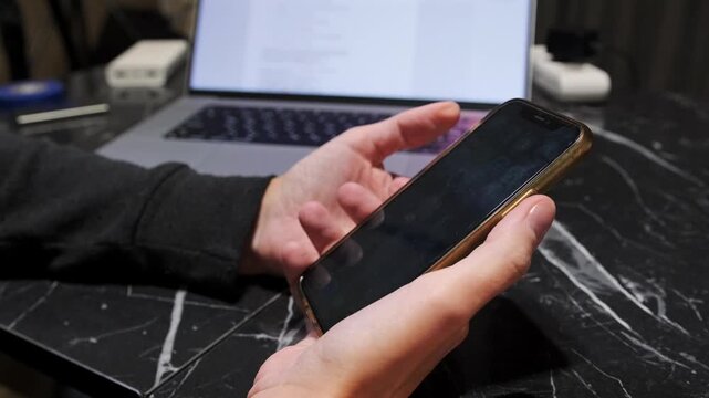Hand pressing smartphone buttons to take screenshot, close-up of capturing screen image on mobile device during everyday usage near laptop on desk. Taking screenshot on phone using buttons