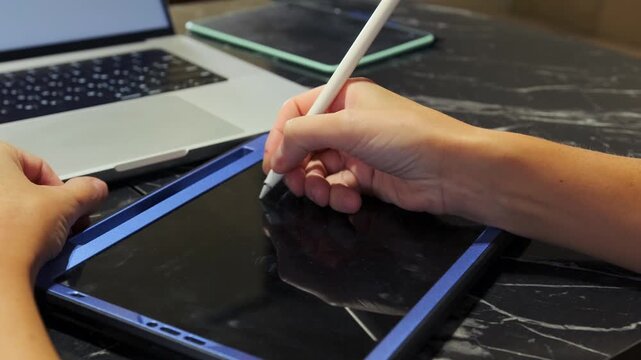 Close-up of hand writing on tablet screen with stylus pen, precise digital input for notes or drawing, modern creative workflow and touchscreen interaction in home or office setting