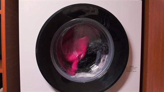 washing machine rinsing clothes front view, rotating drum with water and foam during rinse cycle, fabric moving continuously inside appliance, household laundry process and cleaning operation at home