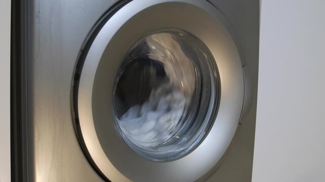 washing machine spinning clothes close-up view, high speed spin drying removing moisture from fabric, rotating drum during final cycle, household appliance operation, efficient laundry process