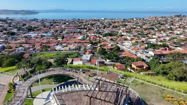 Dona C&eacute;lia viewpoint, Iguaba Grande &ndash; aerial drone backward shot revealing cityscape, cinematic 4K, clear blue sky, wide-angle aerial view, travel destination in Regi&atilde;o dos Lagos, urban skyline.