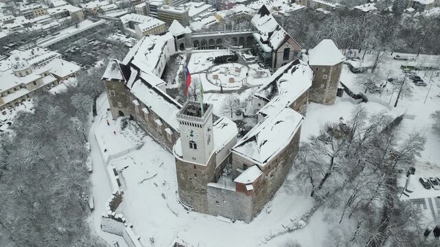 Aerial orbit of snowy Ljubljana Castle with city skyline in background, Ljubljana, Slovenia.