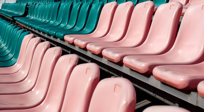 Empty pink and green plastic chairs arranged in diagonal rows on metal bleacher structures provide spectator seating within an outdoor sports arena or public venue.