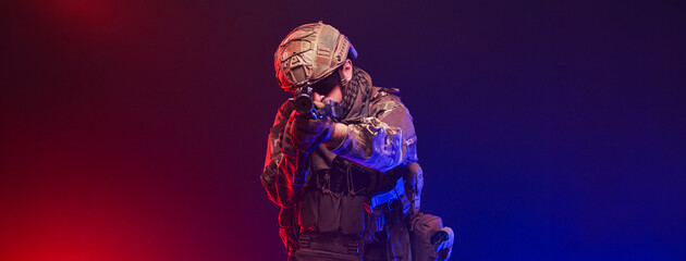 Naklejka premium Tactical soldier on blurred red and blue studio background. Concept defense and modern warfare. 