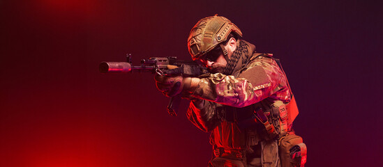 Naklejka premium Soldier holding rifle on red background with atmospheric smoke. Concept conflict and strength. 