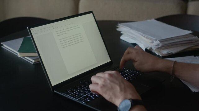 Close up of unrecognizable hands of mature adult male author writing novel on laptop at table in living room