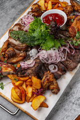 Assorted grilled meats with chicken wings, beef steak slices, roasted potato wedges, fresh onion...