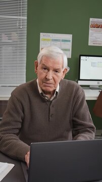 Vertical shot of senior man using laptop and smiling looking at camera in computer class at retirement home, story format