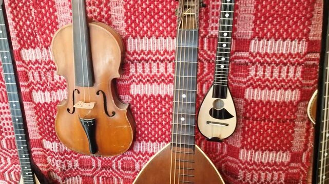 Traditional Cretan musical instruments in Rethymno antique shop. Collection of mandolins and violins on red embroidered carpet background. Authentic Greek artisan craft and musical heritage 4k.