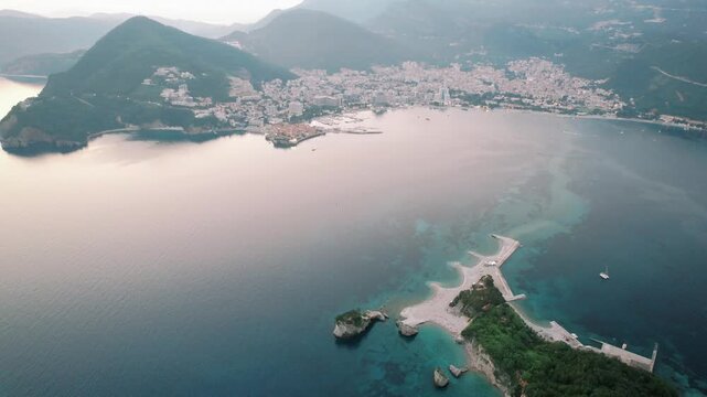 Sunrise drone view. Aerial perspective of tranquil bay at sunrise highlighting rocky islet and charming town