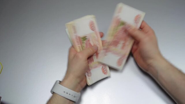 Man counts red paper 5000 rubles bills on a gray background top view. Russian cash money in male hand. A man holds a wad of money in his hands. A close-up of a man's hands counts a bundle of bills. 