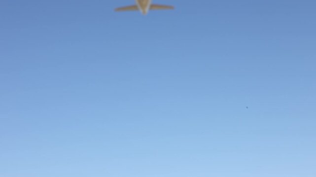 A passenger airplane flying in a clear blue sky. View of the airplane from below showing its underside.