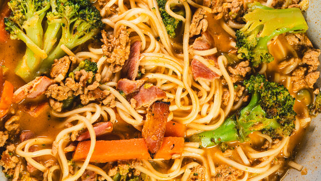 Creamy noodles with minced beef, bacon and vegetables including broccoli, served in a bowl. Rich texture and warm comfort food presentation.