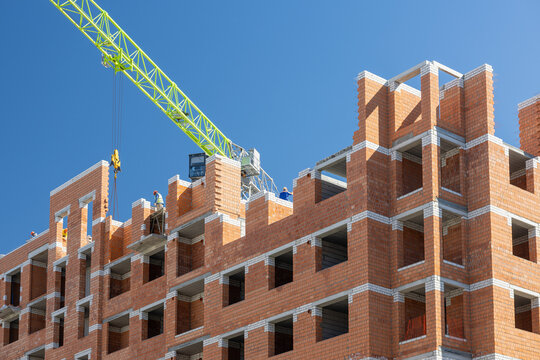 Brick apartment building under construction with tower crane and workers