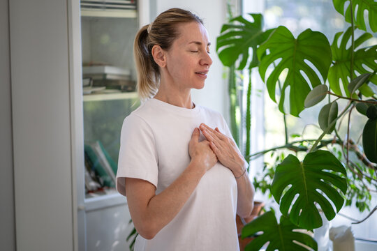 Smiling happy mature woman doing self care stress relief deep breathing exercise for relaxation, positive female with hands on chest practicing mindfulness and calmness, zen therapy for mental health.