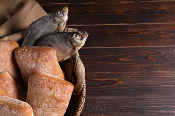 Obraz premium Fresh loaves of bread and dried fish in wicker basket on wooden table, top view. Space for text
