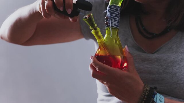 Girl Lights A Smoking Colorful Bong With Dry CBD Cannabis And Smokes It With Thick Smoke For Calmness Of The Nervous System