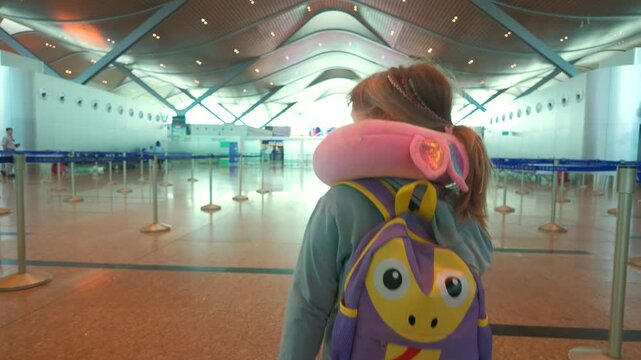 Child with a backpack and neck pillow in an empty airport terminal during a travel morning