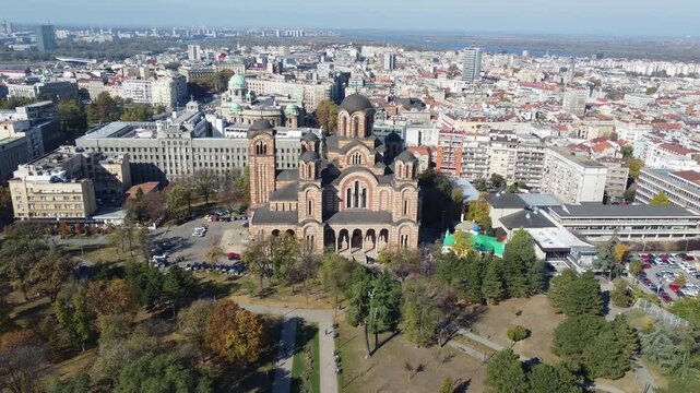 Cinematic aerial drone shot moving backwards from the iconic Saint Mark's Orthodox Church, slowly revealing the wide urban panorama and skyline of Belgrade, Serbia, during a bright and sunny day.