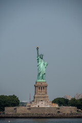 Fototapeta premium New york, usa august 16,2024. Statue of liberty on liberty island rising above new york harbor with manhattan skyline in the distance, clear daytime sky