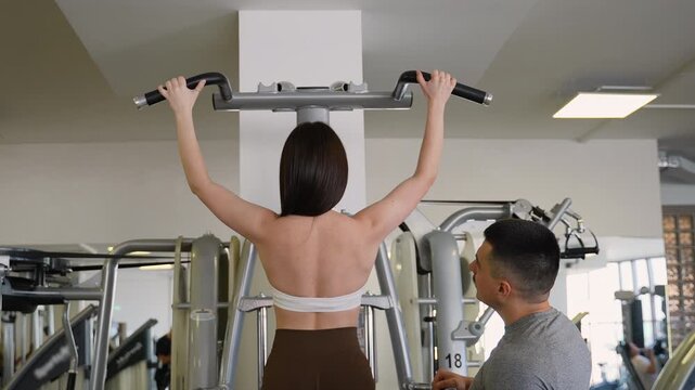 Personal trainer supervising woman doing pull ups on a machine