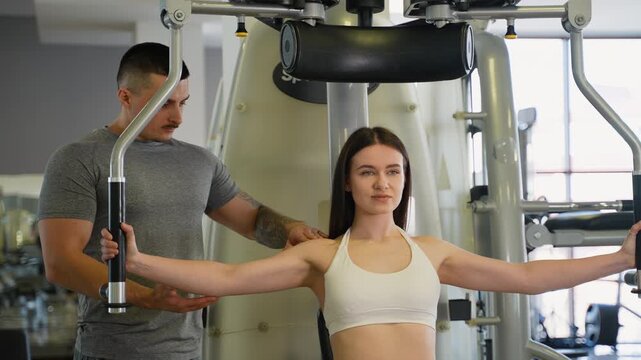 Personal trainer assisting woman with chest fly machine workout