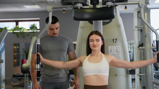 Personal trainer supervising woman on chest fly machine