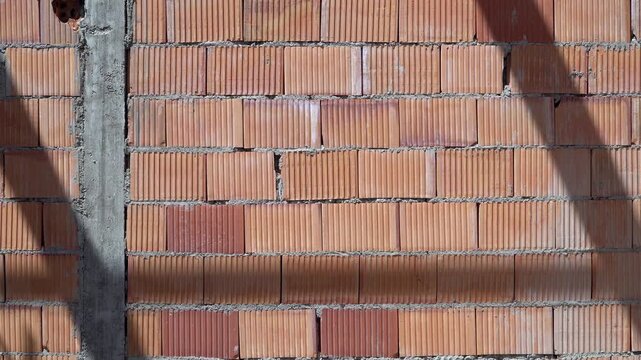 Close-up shot of a wall made from red hollow clay blocks at a construction site. The wall is brightly illuminated by direct sunlight, highlighting the texture and pattern of the building material.