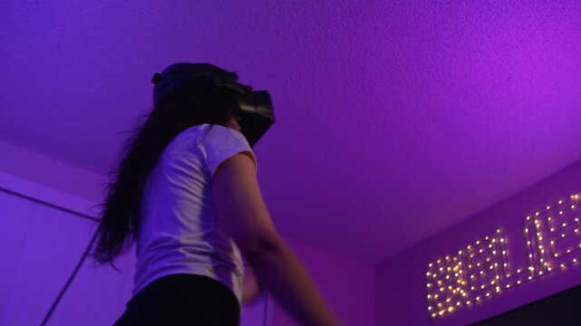Woman playing virtual reality game with controllers in neon light room using modern technology for entertainment and full immersion into digital environment