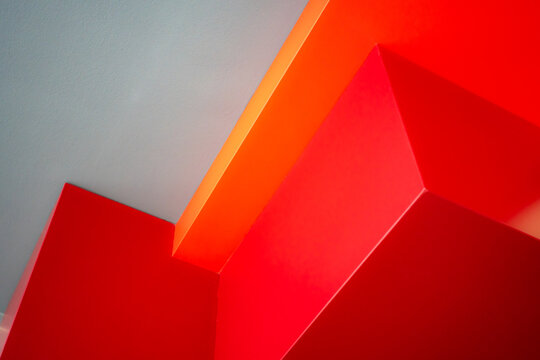Red and orange architectural planes with smooth surfaces and sharp angles intersect in an abstract geometric composition.