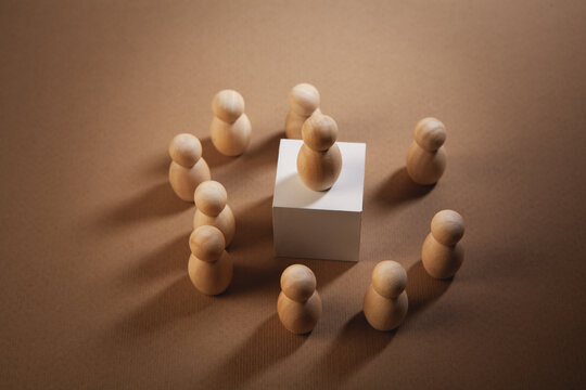 Wooden figures of people around a cube on a brown background.