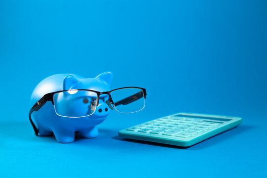 Blue piggy bank with glasses and calculator on a blue background.