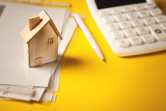 Wooden house model, calculator and pen on yellow background. Home loan concept