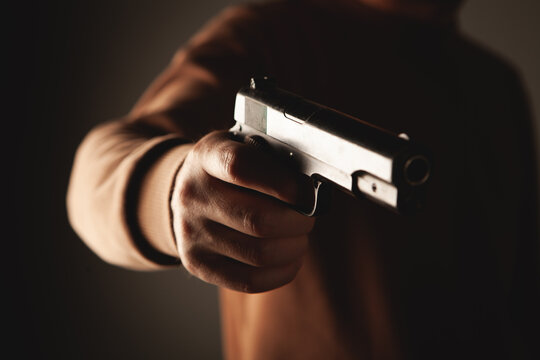 Man with gun in hand on dark background, closeup. Criminal concept