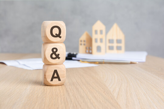 Stacked wooden blocks with Q and A text and blurred house models.