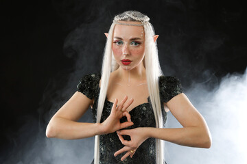 Naklejka premium Beautiful girl dressed as elf on black background with smoke