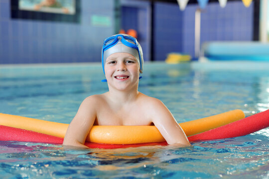 Cute little boy swimming with water noodles during lesson in pool