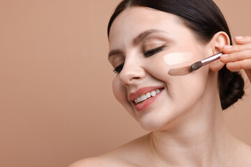 Fototapeta premium Woman applying makeup on her face with brush against beige background, closeup. Space for text