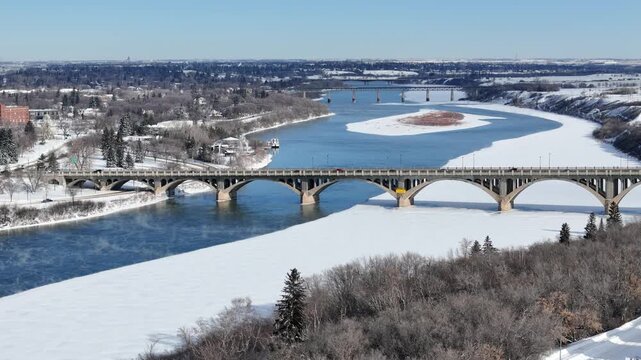 Aerial drone footage captures a bridge spanning a river with snow