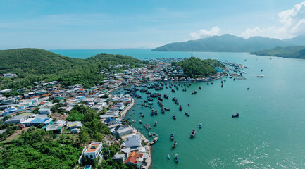 Obraz premium An aerial view of a coastal village in Hon Mieu, Nha Trang, Vietnam, with numerous fishing boats docked in the turquoise bay. The village is nestled between lush green hills and the sea.