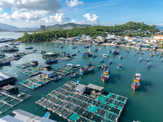 A scenic aerial view of a bustling fishing village in Hon Mieu, Nha Trang, Vietnam, showcasing numerous boats and floating fish farms. © Zenstratus