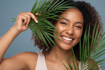 Naklejka premium Young black woman peeking through green palm leaves smiling